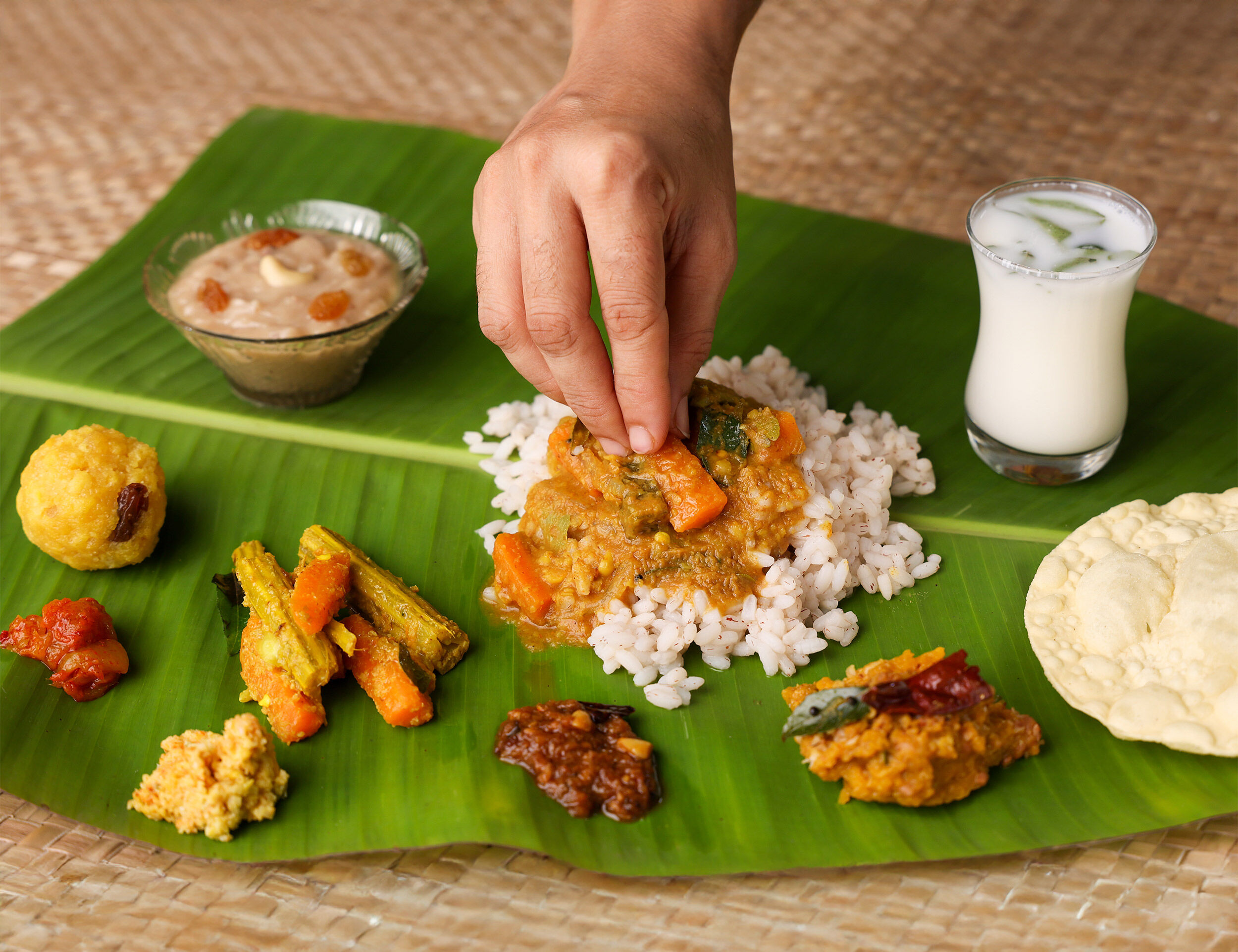 Hand mixing traditional Onam Sadhya meal served on a banana leaf with rice, avial, payasam, papadam, and buttermilk